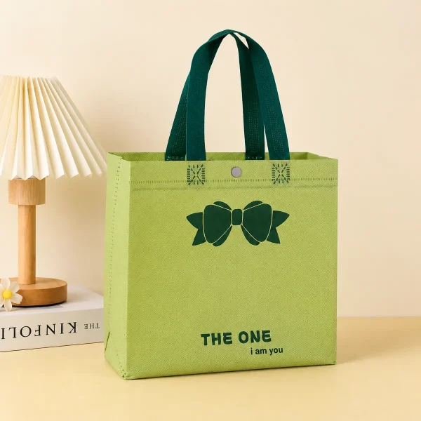 Green affordable gift bag with contrasting dark green loop handles, bow print and The One text, on a pale yellow background.