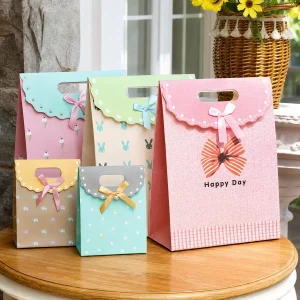 Pastel paper gift bags in pink, green, blue and yellow with flap closures and ribbon bows, on a wooden table.