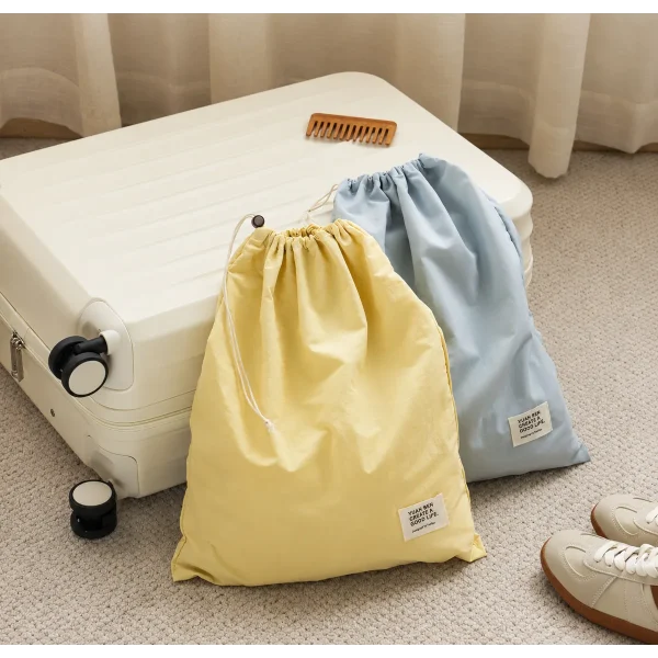 Pale yellow and light blue waterproof nylon drawstring bags with cord closures and small labels, beside a suitcase.