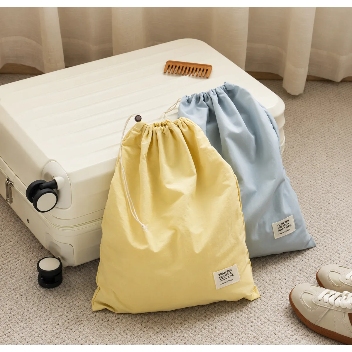 Pale yellow and light blue waterproof nylon drawstring bags with cord closures and small labels, beside a suitcase.