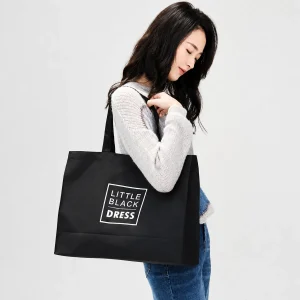 Black polyester Oxford carry bag with long black handles and white boxed lettering, carried on a woman's shoulder.